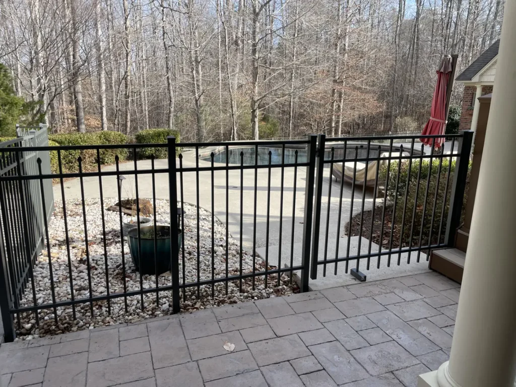 Black aluminum pool fence and gate installed around a backyard patio