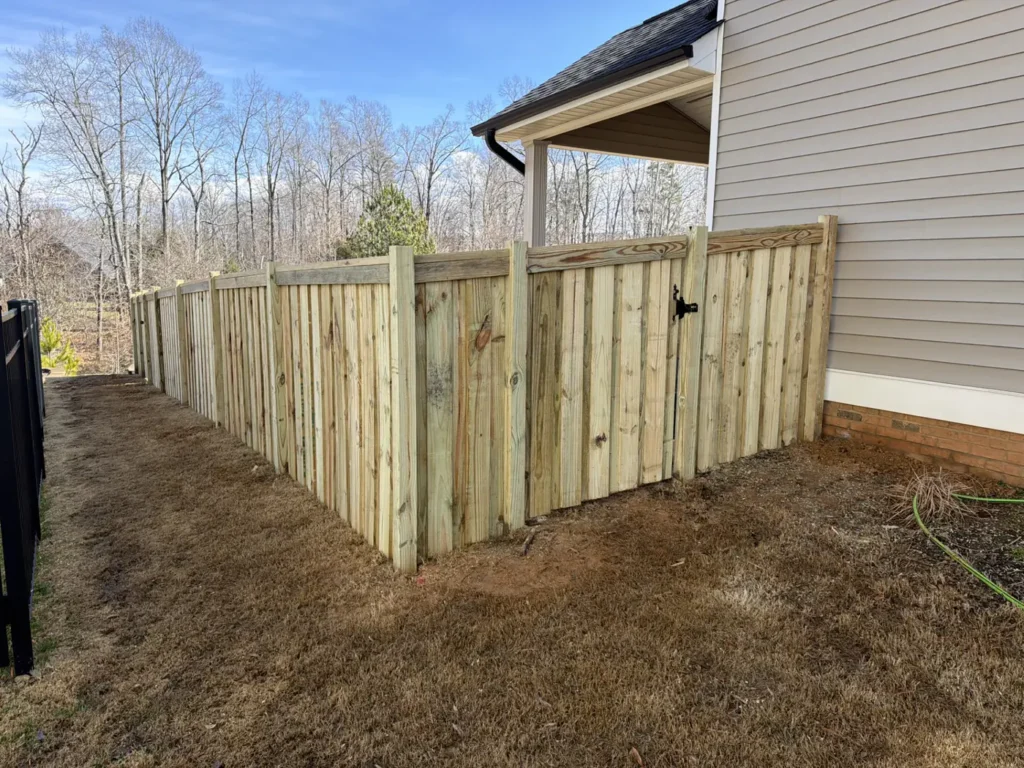 New wood privacy fence with a walk gate along a tree line