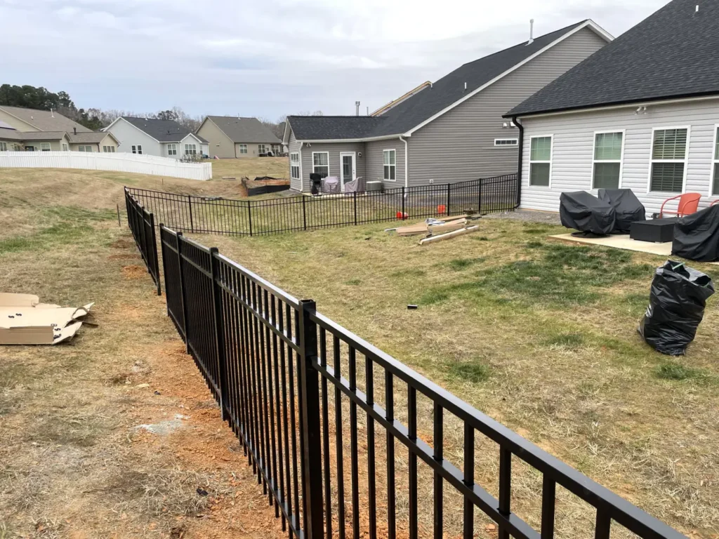 Black aluminum fence being installed along a long run behind a new home