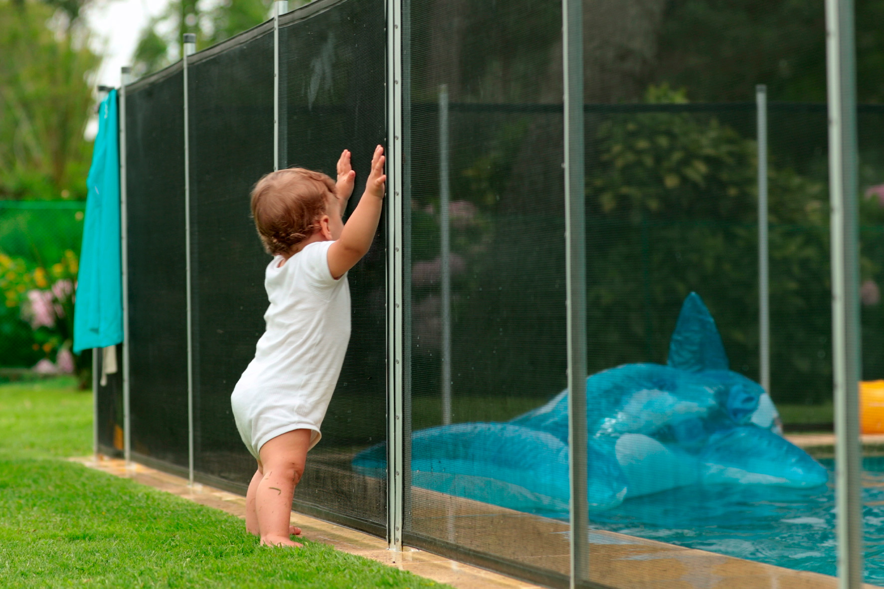 Toddler reaching up against a mesh pool safety fence