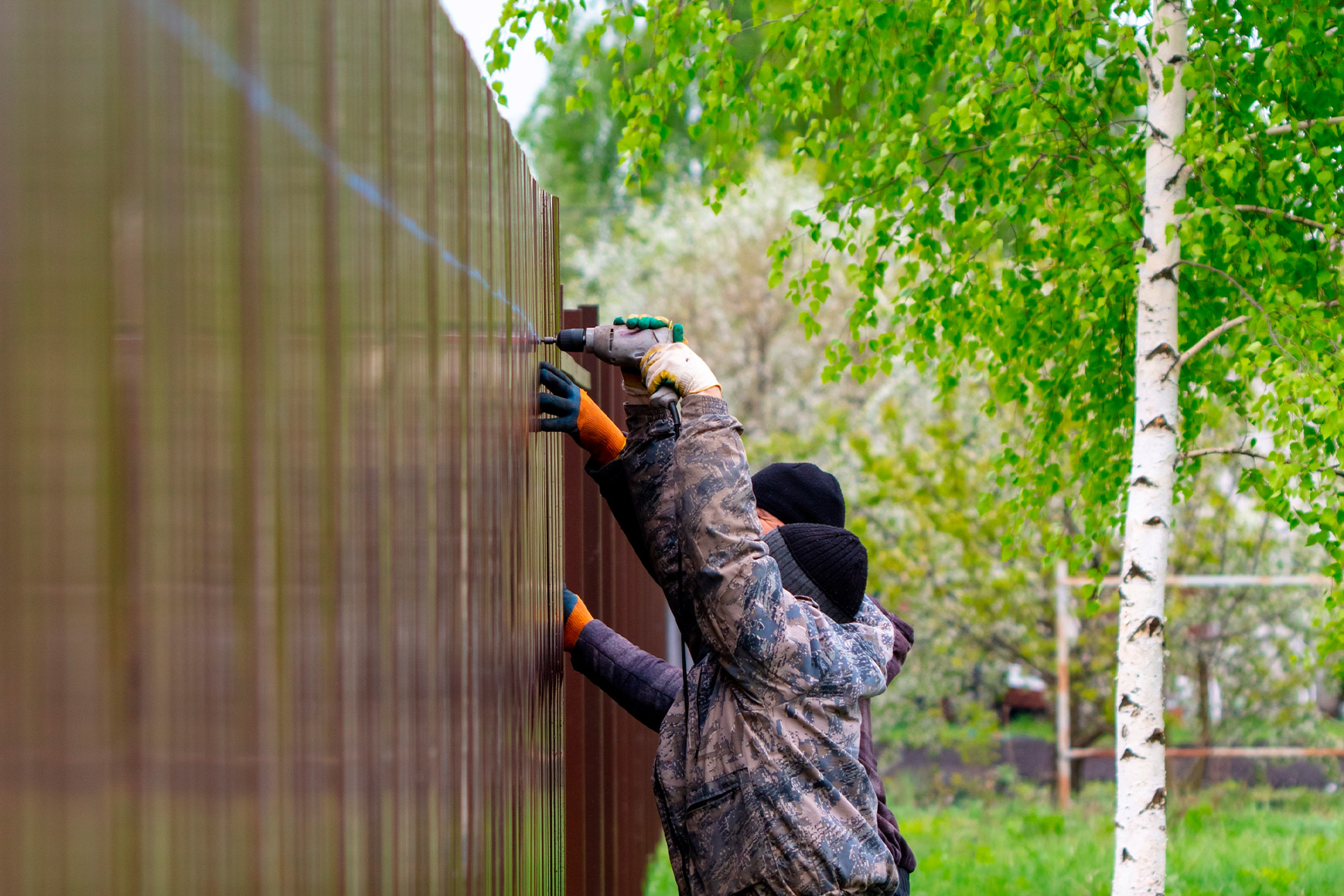 Two installers fastening boards to a tall wood privacy fence in a backyard