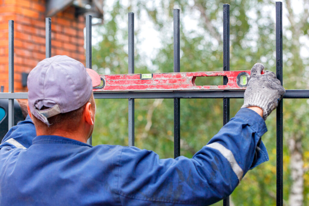 Installer checking a black metal fence panel with a level