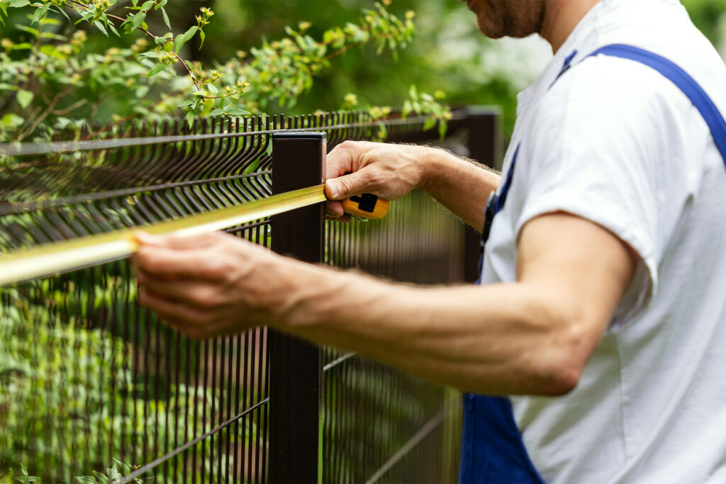 Installer measuring a welded wire fence panel with a tape measure