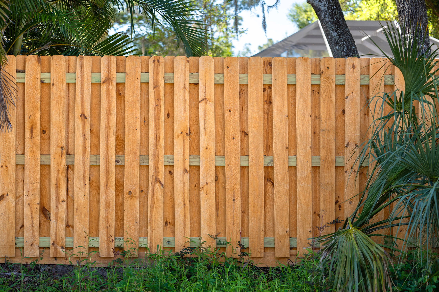 A rustic wooden fence with evenly spaced vertical boards, surrounding a garden.