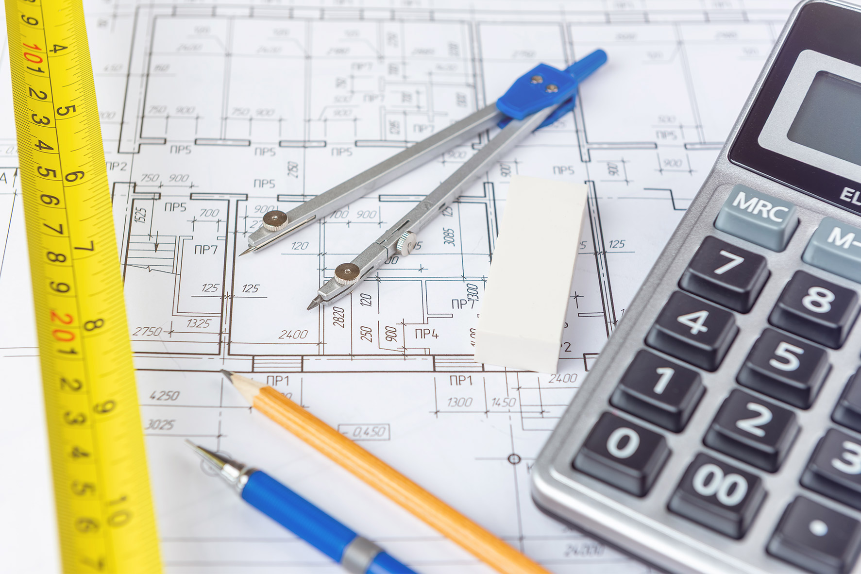 A detailed architectural blueprint with a yellow tape measure, a compass, an eraser, a pencil, a pen, and a calculator, conveying precision and planning.