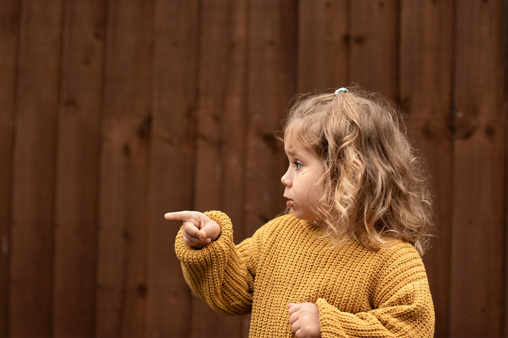 A little girl excitedly pointing at an object off-screen, showcasing her curiosity and engagement with her surroundings.