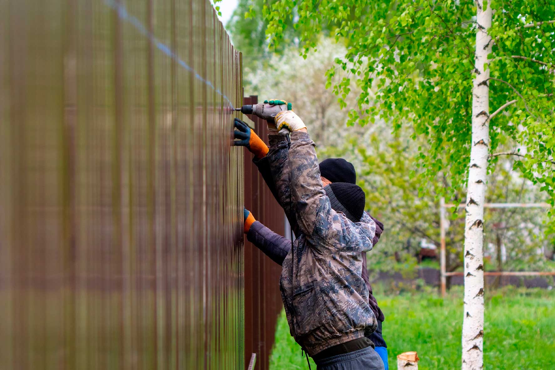 Two men installing a wooden fence, illustrating a step in the New Homeowner's Guide to Property Fencing.