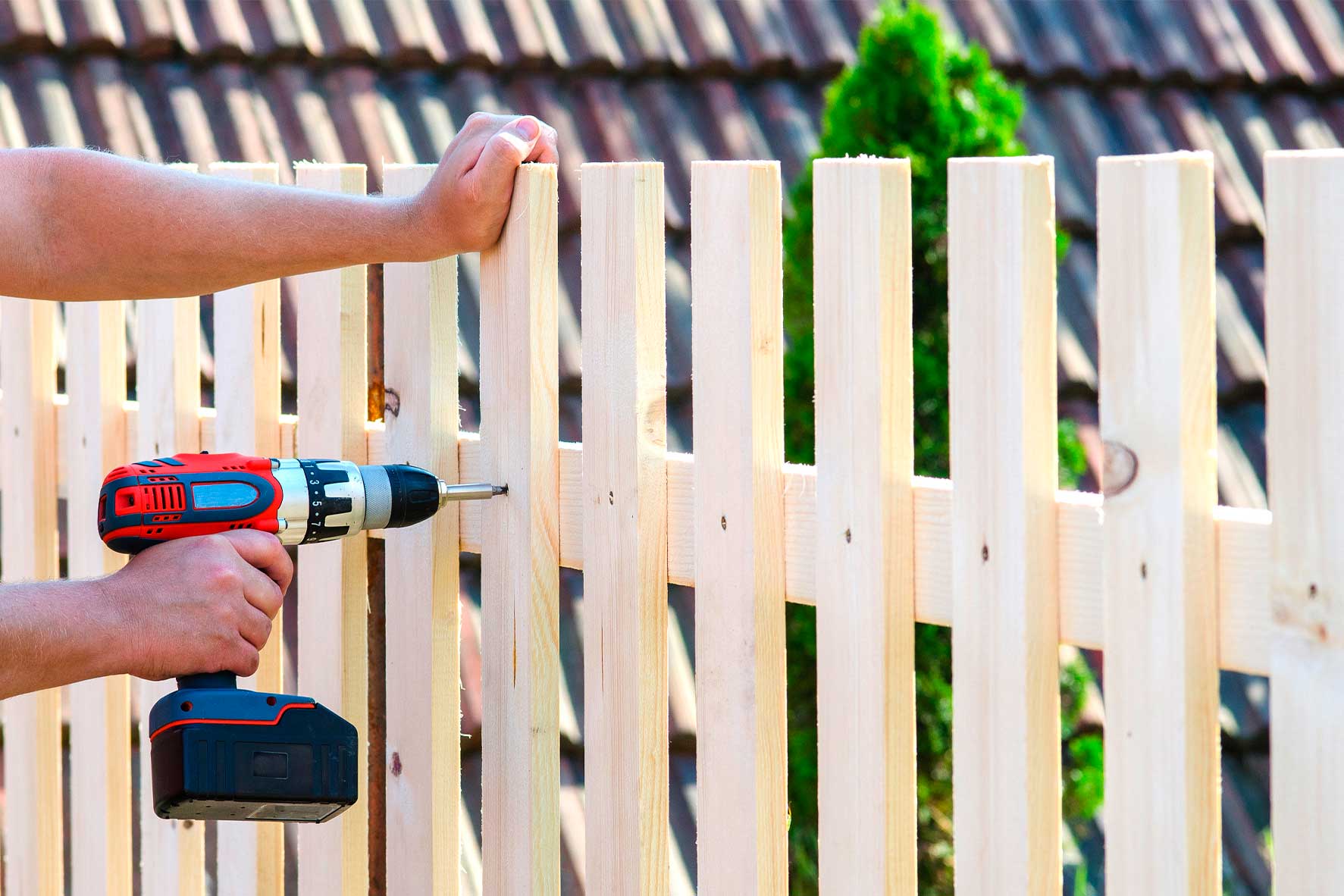 A man drills into wood while constructing a fence, illustrating a step from the New Homeowner's Guide to Property Fencing.