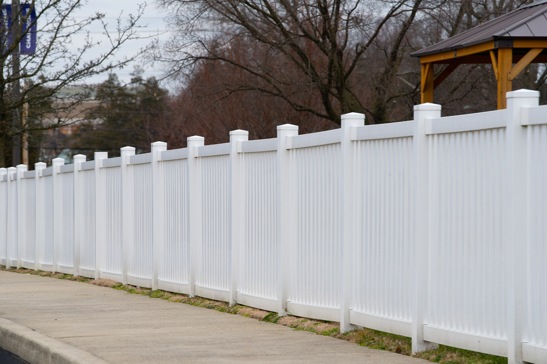A white vinyl fence is located next to a sidewalk, showcasing the quality of premium vinyl versus big box alternatives.