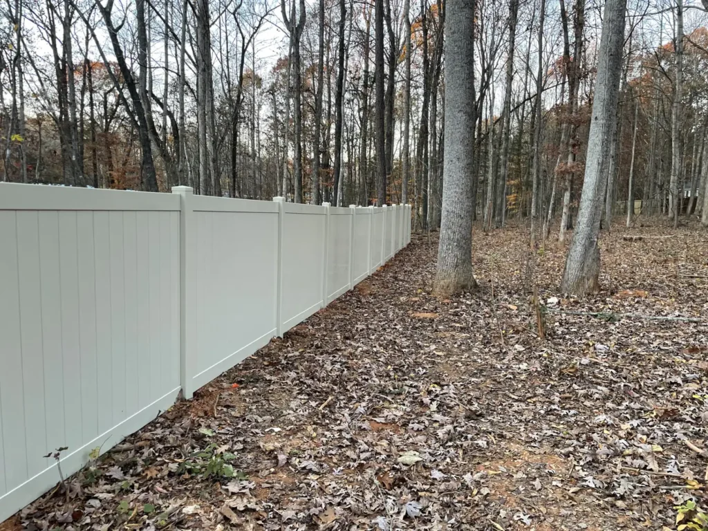 Tall white vinyl privacy fence with smooth panels along a wooded backyard