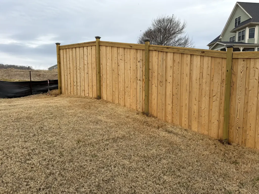 Tall wood privacy fence with a flat face and cap rail around a new-build backyard