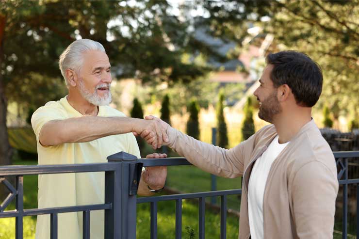 Friendly relationship with neighbours. Happy men shaking hands above fence outdoors