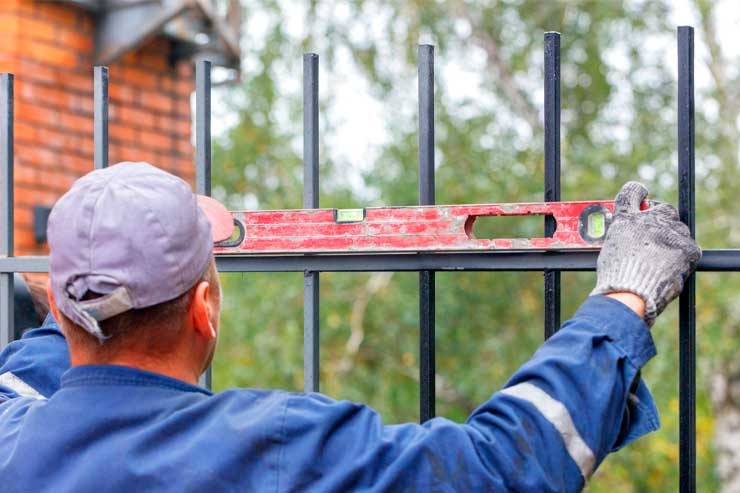 Fence installer checking a black metal fence panel with a level to keep the line straight