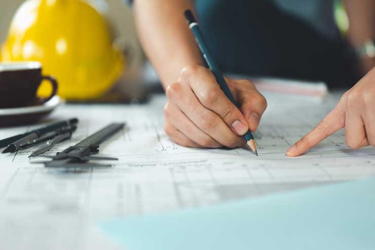 Hands sketching a property layout on a site plan beside a hard hat
