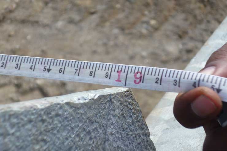 Tape measure extended across a stone edge while measuring a fence line