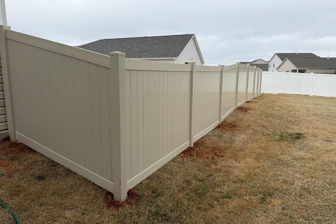 A beige fence lines a grassy yard, separating it from neighboring houses under a cloudy sky, creating a neat boundary.